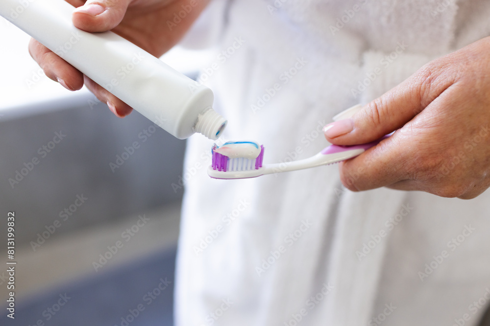 At home, mature Caucasian woman putting toothpaste on toothbrush At home, mature Caucasian woman putting toothpaste on toothbrush
