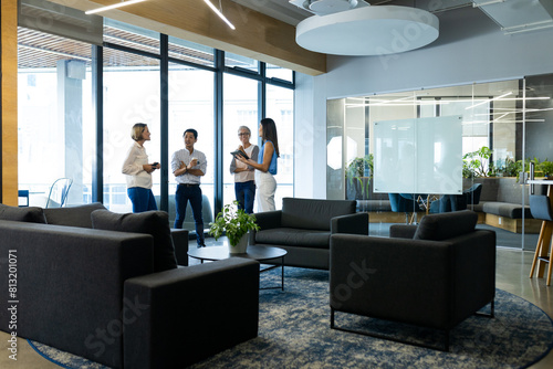 Diverse team standing, talking in modern office lounge, copy space