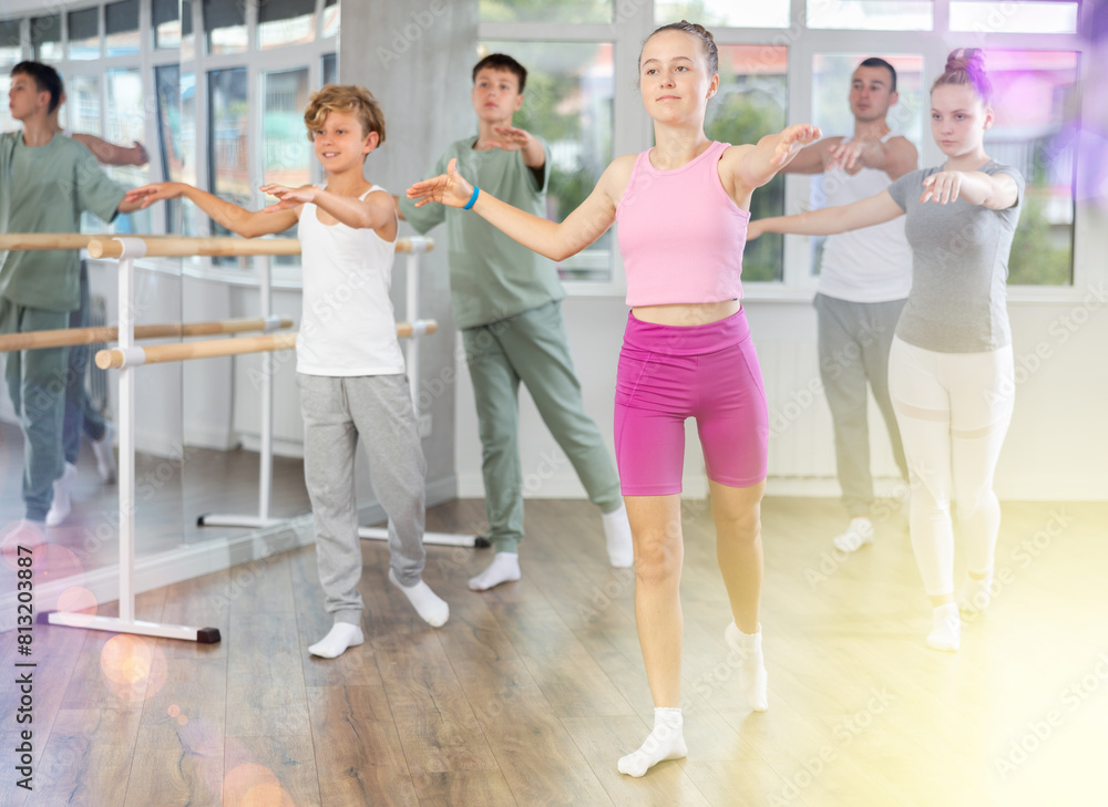 Fototapeta premium Gracious teen girl doing choreography in group with instructor during ballet classes in dance studio
