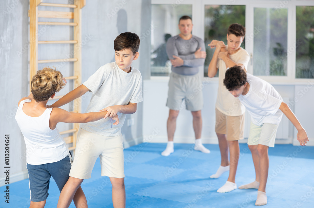 Determined motivated teenagers sparring during group self-defense training with male instructor, practicing basic techniques