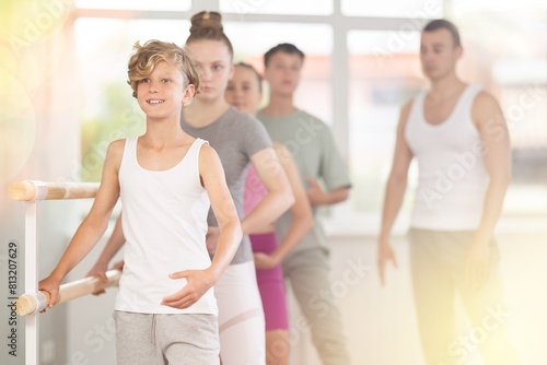 Teen boy participate in training, performs exercises, third position during group lesson. Young students engaged in ballet studio, perform repetitions of elements under male teacher guidance.
