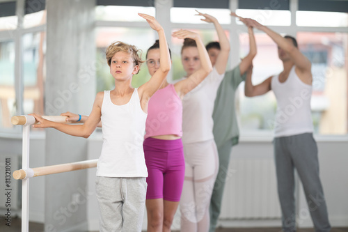 Fototapeta Naklejka Na Ścianę i Meble -  Teen boys and girls participate in training, performs exercises, third position. Young students engaged in ballet studio, perform repetitions of elements and tasks under male teacher guidance.