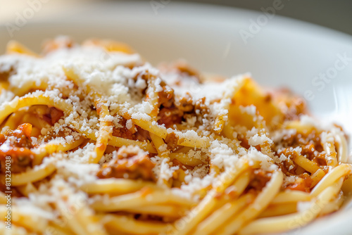 A close-up image of a classic Italian pasta bolognese, served in a deep, elegant white dish. Focus on the glossy texture of the sauce and the sprinkling of freshly grated Parmesan cheese on top. 
