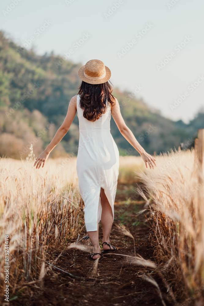 Woman in a white sundress and straw hat walks gracefully along a path through a wheat field, evoking a sense of freedom and connection with nature. Woman in a white sundress and straw hat walks gracefully along a path through a wheat field, evoking a sense of freedom and connection with nature.