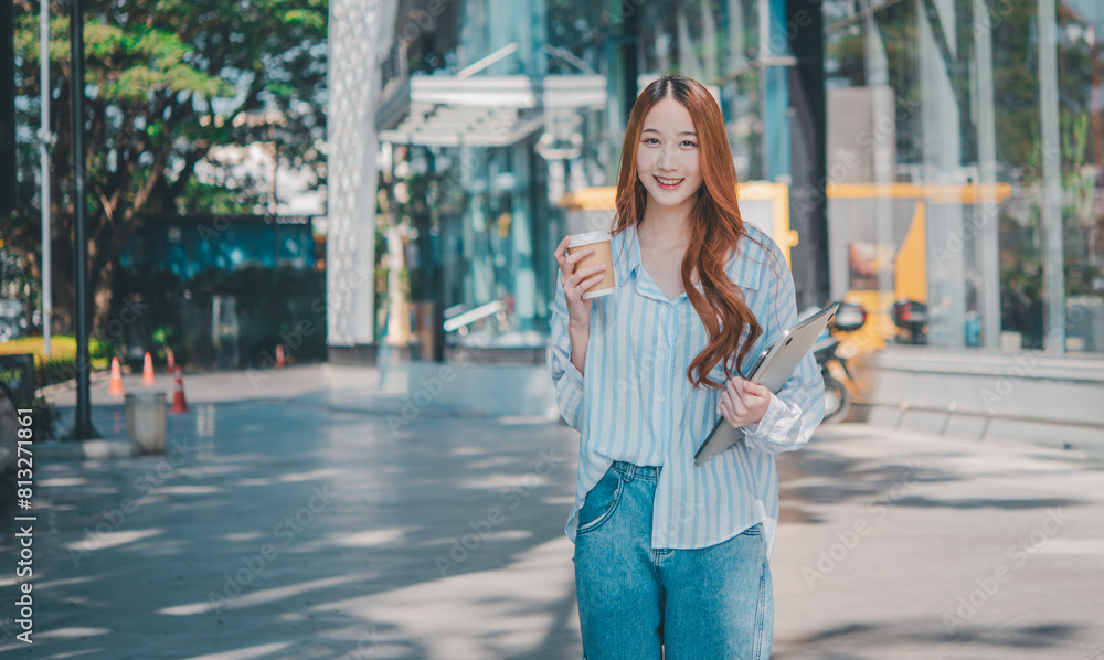Fototapeta premium A woman is walking down a sidewalk holding a cup of coffee and a clipboard