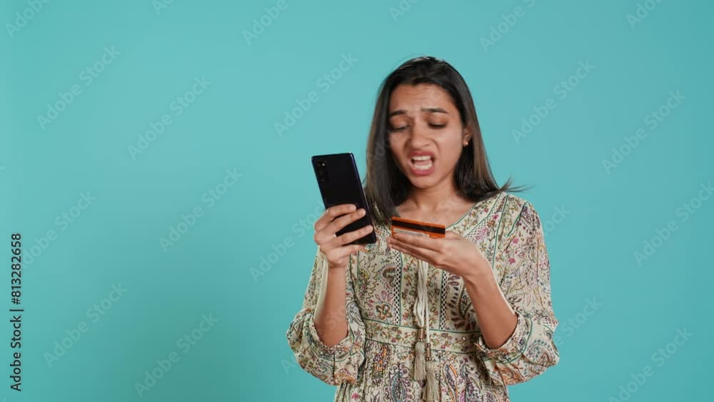 Woman adding payment method on shopping website using phone, taking advantage of promotions, studio background. Indian person buying stuff online using credit card, typing data on device, camera A Woman adding payment method on shopping website using phone, taking advantage of promotions, studio background. Indian person buying stuff online using credit card, typing data on device, camera A