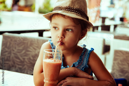 Cute caim thinking kid girl in summer hat drinking tasty juice in street restaurant. Closeup photo