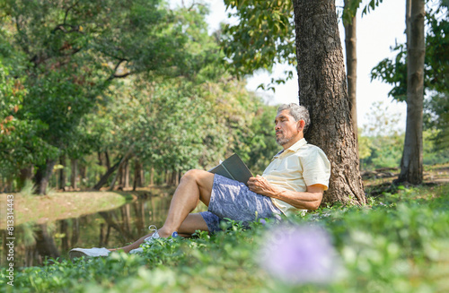 asian senior man fell asleep while reading a book under a tree,older adult resting in the nature park,concept of elderly people lifestyle,hobbies,relaxing in nature © Verin