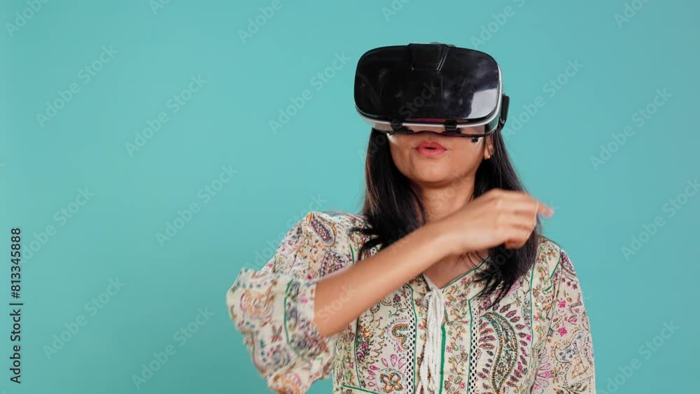 Indian woman wearing virtual reality headset, doing swiping gestures. Technology enthusiast using high tech futuristic modern VR gadget, isolated over studio background, camera B Indian woman wearing virtual reality headset, doing swiping gestures. Technology enthusiast using high tech futuristic modern VR gadget, isolated over studio background, camera B