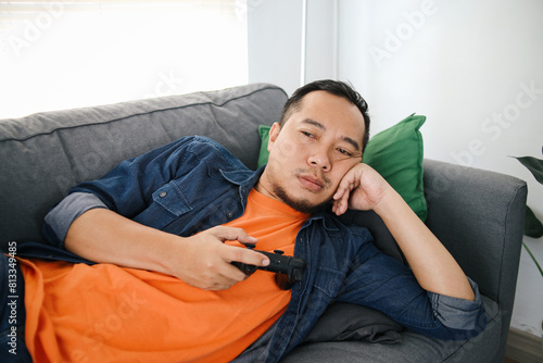 Bored man holding joystick, playing video games while lying on sofa at home