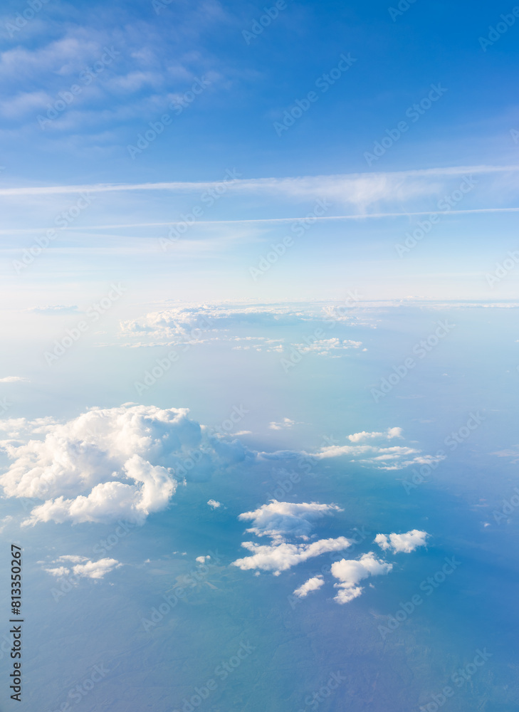 Fototapeta premium Aerial view from airplane window above green ground. View from the airplane window with beautiful clouds at sunrise