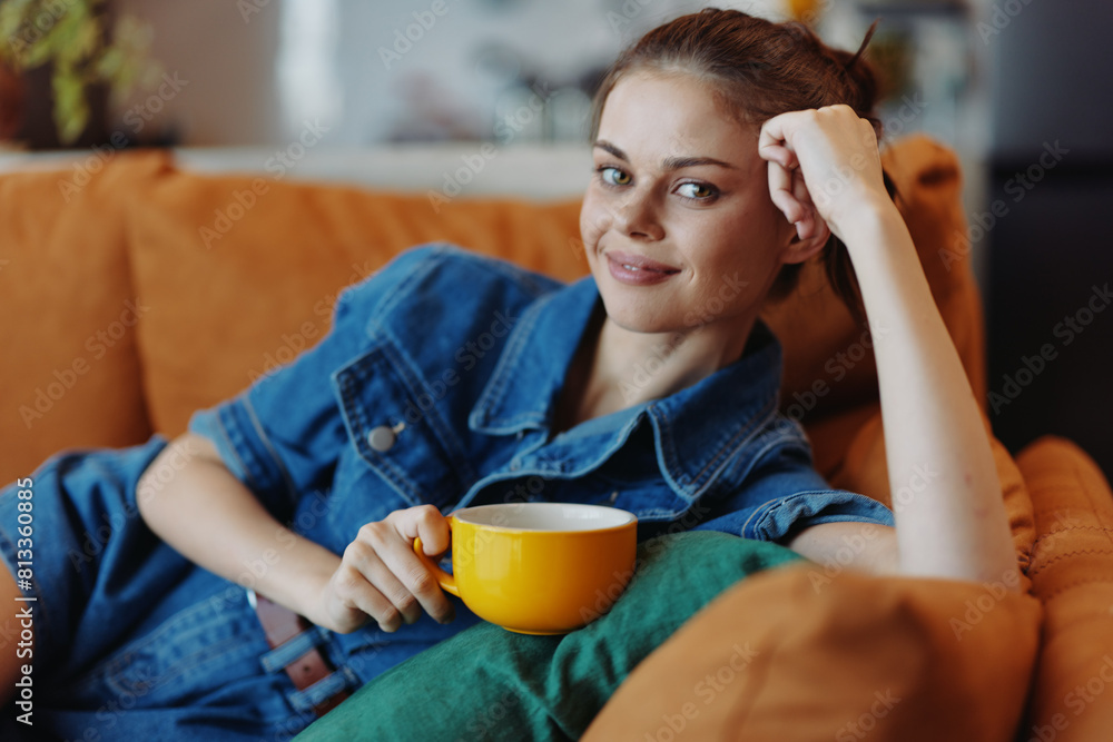 Attractive young woman in stylish denim shirt enjoying coffee while relaxing on comfortable sofa at home Attractive young woman in stylish denim shirt enjoying coffee while relaxing on comfortable sofa at home