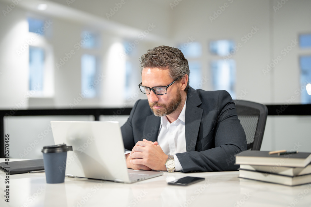 Obraz premium Office worker with laptop at office. Ofice employee remote working in modern office. Serious Businessman on remote meeting, working online in offices place. Business man using computer in office.