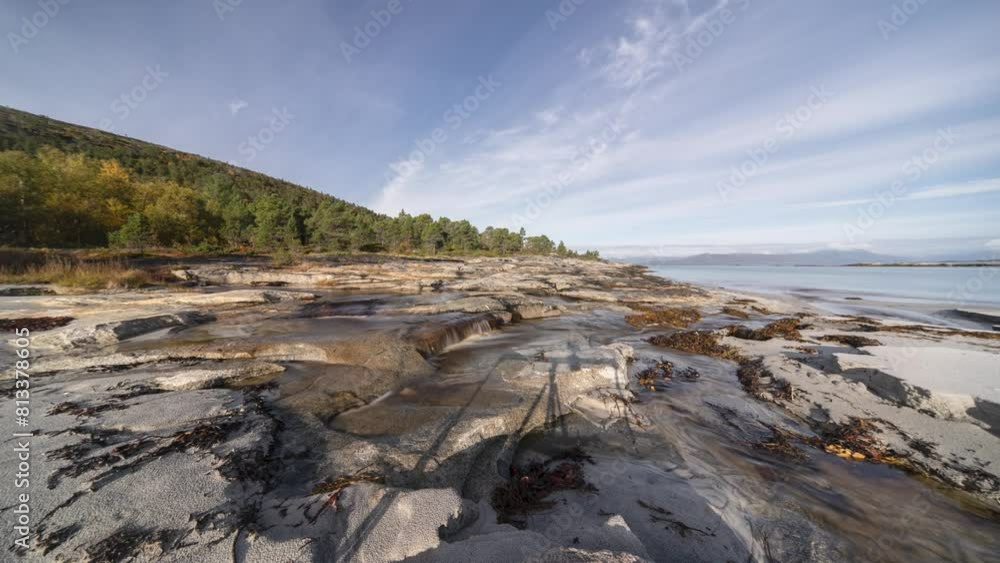 The smooth rocky shore connects to a sandy beach covered by kelp and seaweed as waves roll slowly in the background Timelapse video.
