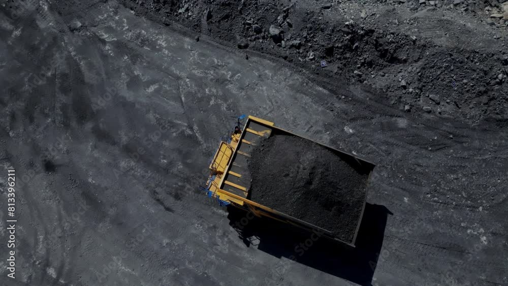 Close-up aerial view of a loaded yellow dump truck on a coal mine's textured black surface Close-up aerial view of a loaded yellow dump truck on a coal mine's textured black surface