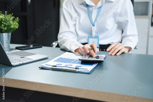 Businesswoman using a calculator to calculate the numbers of statistic business profits growth rate on documents graph data, desk in the office.