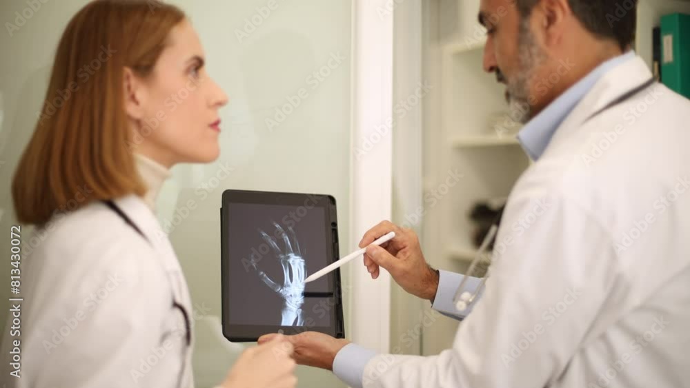 Medical professionals assess an x-ray on a tablet in a clinical environment Medical professionals assess an x-ray on a tablet in a clinical environment