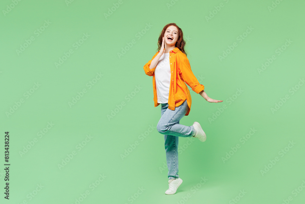 Full body side profile view young ginger woman she wearing orange shirt white t-shirt casual clothes put hand on face raise up leg isolated on plain pastel light green background. Lifestyle concept. Full body side profile view young ginger woman she wearing orange shirt white t-shirt casual clothes put hand on face raise up leg isolated on plain pastel light green background. Lifestyle concept.
