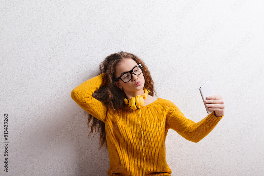 Portrait of a gorgeous teenage girl with curly hair and headphones,taking selfie. Studio shot, white background with copy space. Portrait of a gorgeous teenage girl with curly hair and headphones,taking selfie. Studio shot, white background with copy space.