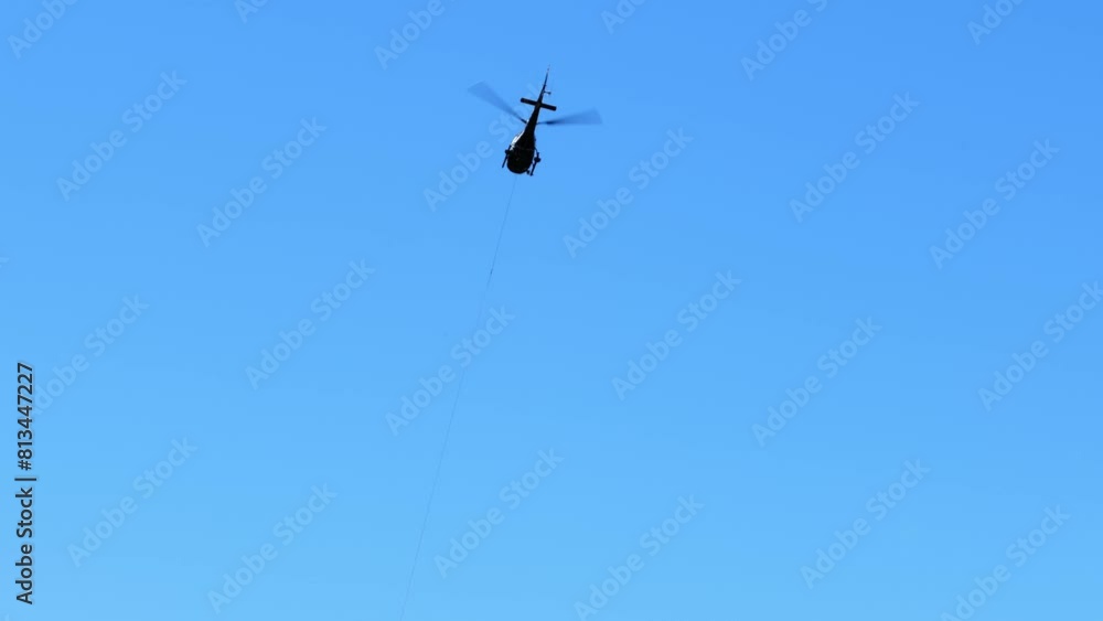 Helicopter Flying Away Against Blue Sky with Hanging Cable over Mountain in a Sunny Day in Switzerland. Helicopter Flying Away Against Blue Sky with Hanging Cable over Mountain in a Sunny Day in Switzerland.