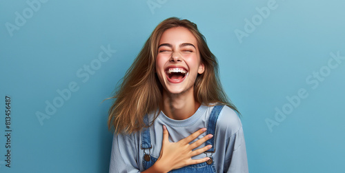 Young caucasian woman isolated on blue background laughs out loudly keeping hand on chest. photo