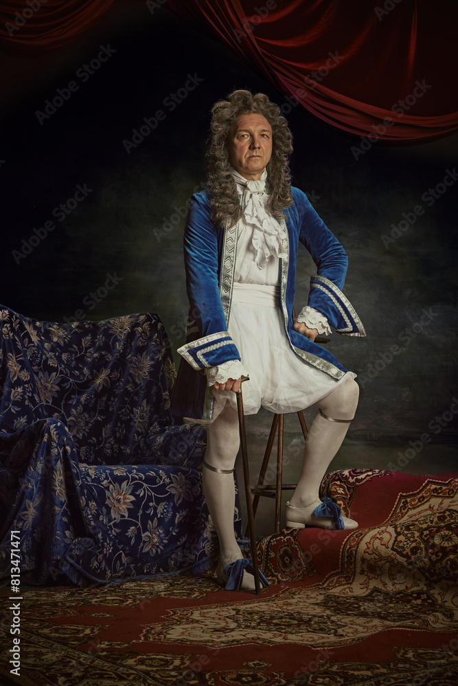 Portrait of elderly man dressed as medieval person, aristocrat with confident expression against vintage studio background. Concept of comparisons of eras, fusion of modernity and history, renaissance Portrait of elderly man dressed as medieval person, aristocrat with confident expression against vintage studio background. Concept of comparisons of eras, fusion of modernity and history, renaissance