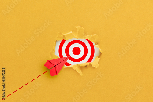 Target concept with red paper plane. Hole in the yellow paper with torn sides and target icon