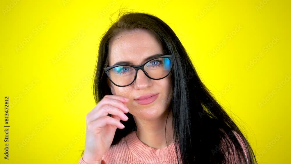 A young beautiful girl, wearing glasses, smiles at the camera on a yellow background. Slow motion. A young beautiful girl, wearing glasses, smiles at the camera on a yellow background. Slow motion.