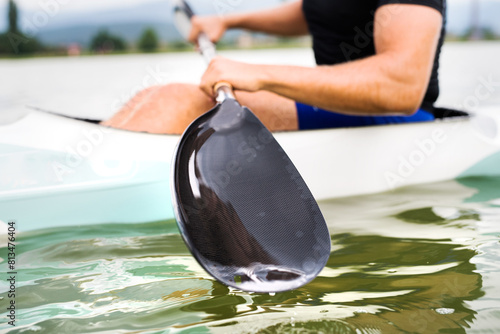 Canoeist man sitting in canoe holding paddle, in water. Concept of canoeing as dynamic and adventurous sport. Rear view, sportman looking at water surface, paddling. Close up. photo