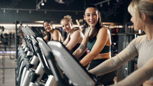 Smiling group of fit young women in sportswear riding on a stationary bikes during a cardio workout class together at the gym photo