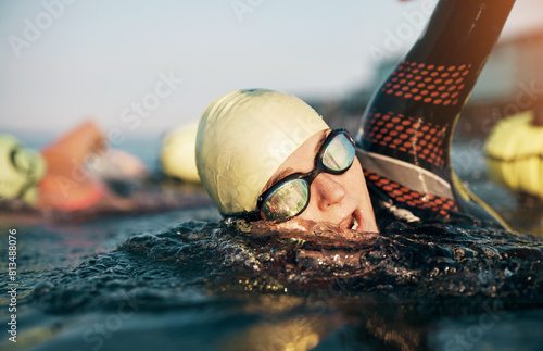 Mature woman and her class doing an open ocean swim together. She wears a wetsuit and swimming goggles while swimming front crawl.