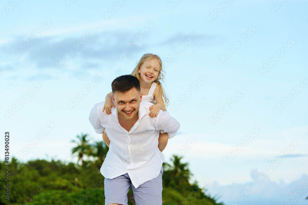 Happy father giving piggyback ride to daughter under sky at sunset Happy father giving piggyback ride to daughter under sky at sunset