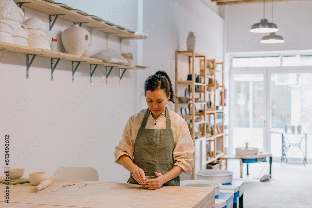 Craftsperson molding shape on clay standing by table at pottery workplace Craftsperson molding shape on clay standing by table at pottery workplace