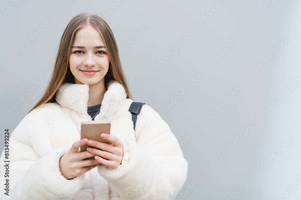Smiling teenage girl using mobile phone in front of white wall Smiling teenage girl using mobile phone in front of white wall