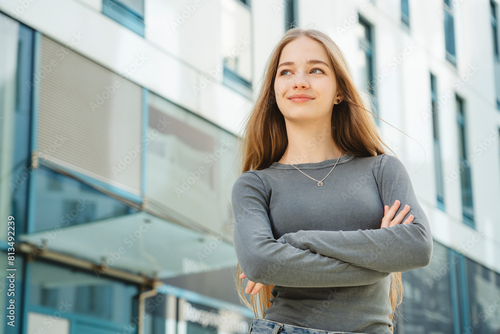 Smiling teenage girl with arms crossed looking away in front of building Smiling teenage girl with arms crossed looking away in front of building