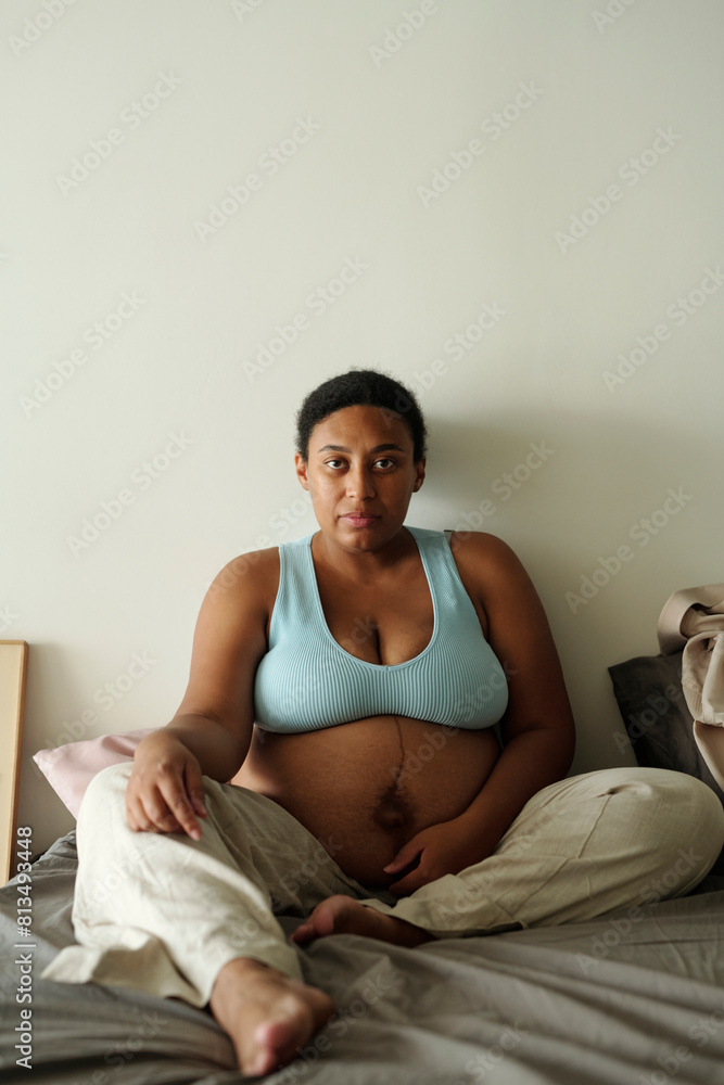 Pregnant woman sitting on bed at home Pregnant woman sitting on bed at home