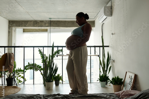 Pregnant woman with hands on stomach at home photo