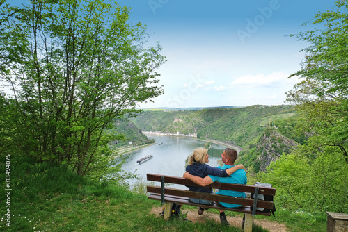 Hiking couple with arms around sitting on bench by view of Loreley Rock in St. Goarshausen, Rhineland Palatinate, Germany photo