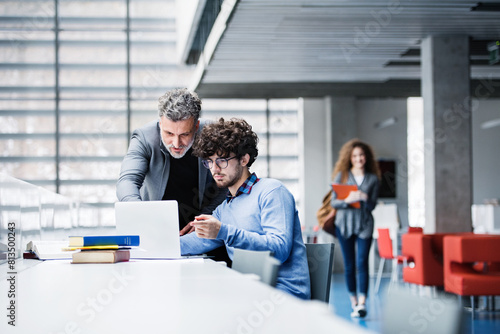 Photos Handsome university professor helping student with final project, showing him research paper, book for thesis in library