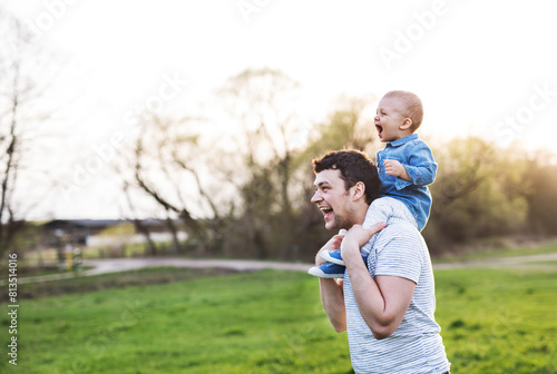 Father carrying little toddler on shoulders, having fun during warm spring day. Father's day concept. © Halfpoint