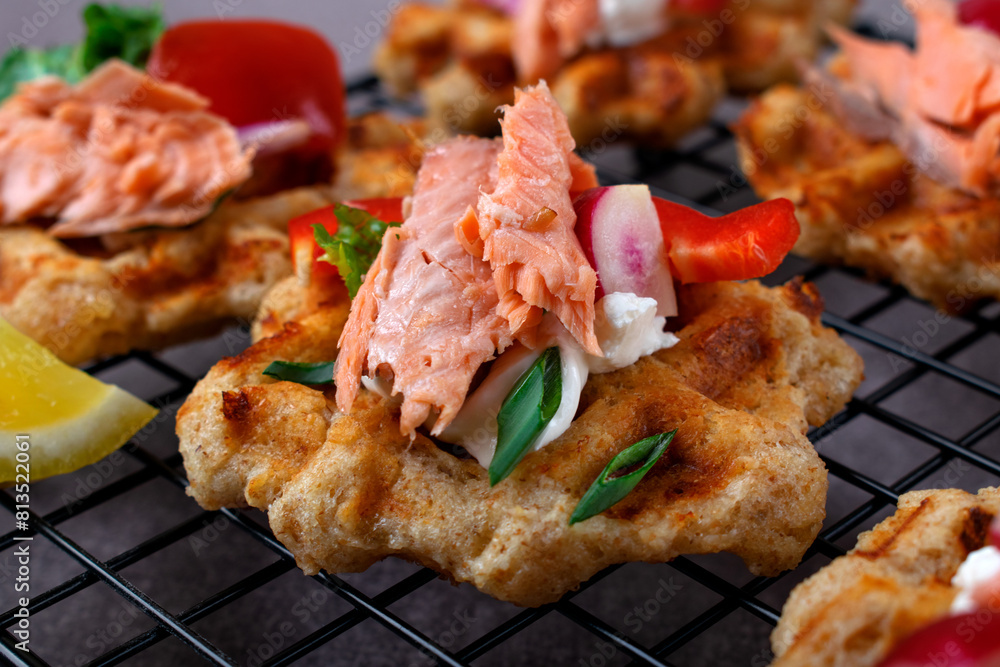 Cheese waffle topped with smoked trout, vegetables and sour cream sauce on the serving rack Cheese waffle topped with smoked trout, vegetables and sour cream sauce on the serving rack