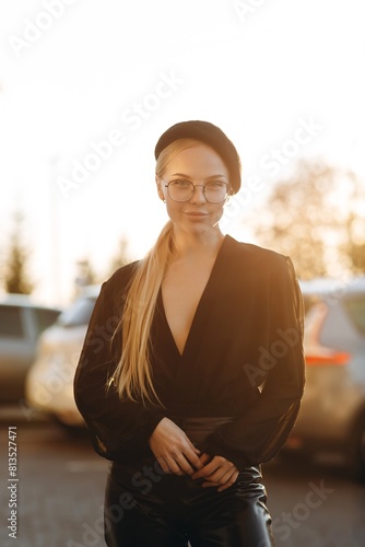 Elegant girl with light daytime make-up and pulled hair, with clear glasses on her eyes and a black beret on her head, looks right at the camera is holding her hands in front, wearing a black blouse