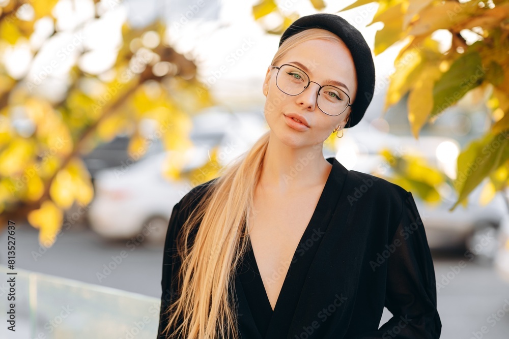 Portrait of a flirtatious girl with light daytime makeup, clear glasses on her eyes and a black beret, wearing a black blouse against a background of yellow-green leaves on a tree Portrait of a flirtatious girl with light daytime makeup, clear glasses on her eyes and a black beret, wearing a black blouse against a background of yellow-green leaves on a tree