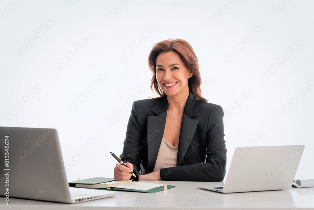 Mid age businesswoman sitting at desk and using laptop against isolated background Mid age businesswoman sitting at desk and using laptop against isolated background