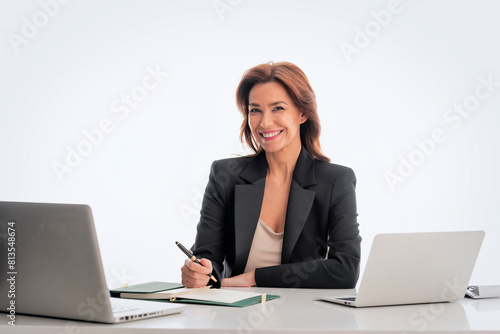 Mid age businesswoman sitting at desk and using laptop against isolated background