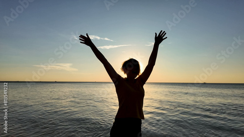 Silhouetted individual with arms raised in celebration at sunset on a tranquil beach, evoking feelings of freedom and summer vacation vibes © fotoworld