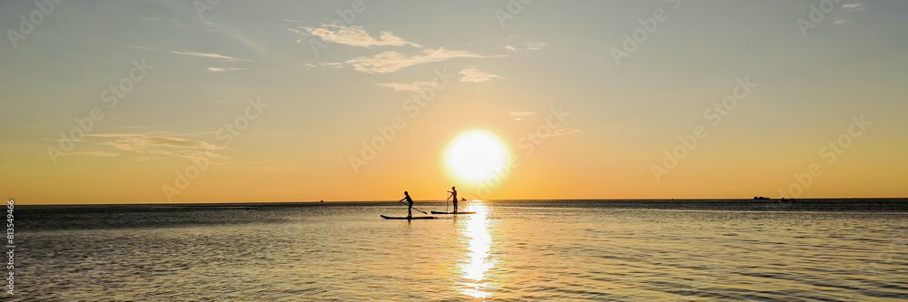 Two people paddleboarding on a calm ocean at sunset, silhouetted against the golden sky  ideal for summer vacations and water sports concepts