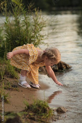 Little girl playing by the water's edge, gentle focus. Symbolizes innocence and the simplest forms of engagement with nature.