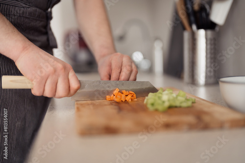 Close-up of hands chopping fresh vegetables on a wooden cutting board in a home kitchen.
