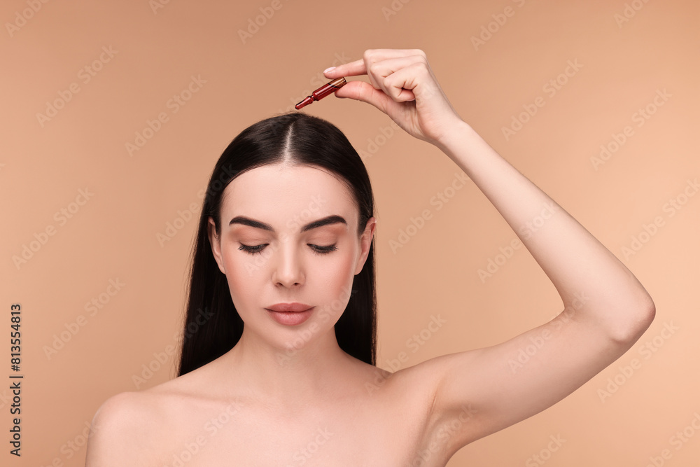 Beautiful young woman using ampoule for hair treatment on beige background Beautiful young woman using ampoule for hair treatment on beige background